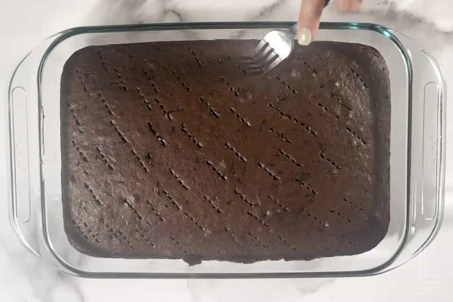 poking holes in a chocolate cake with a fork.