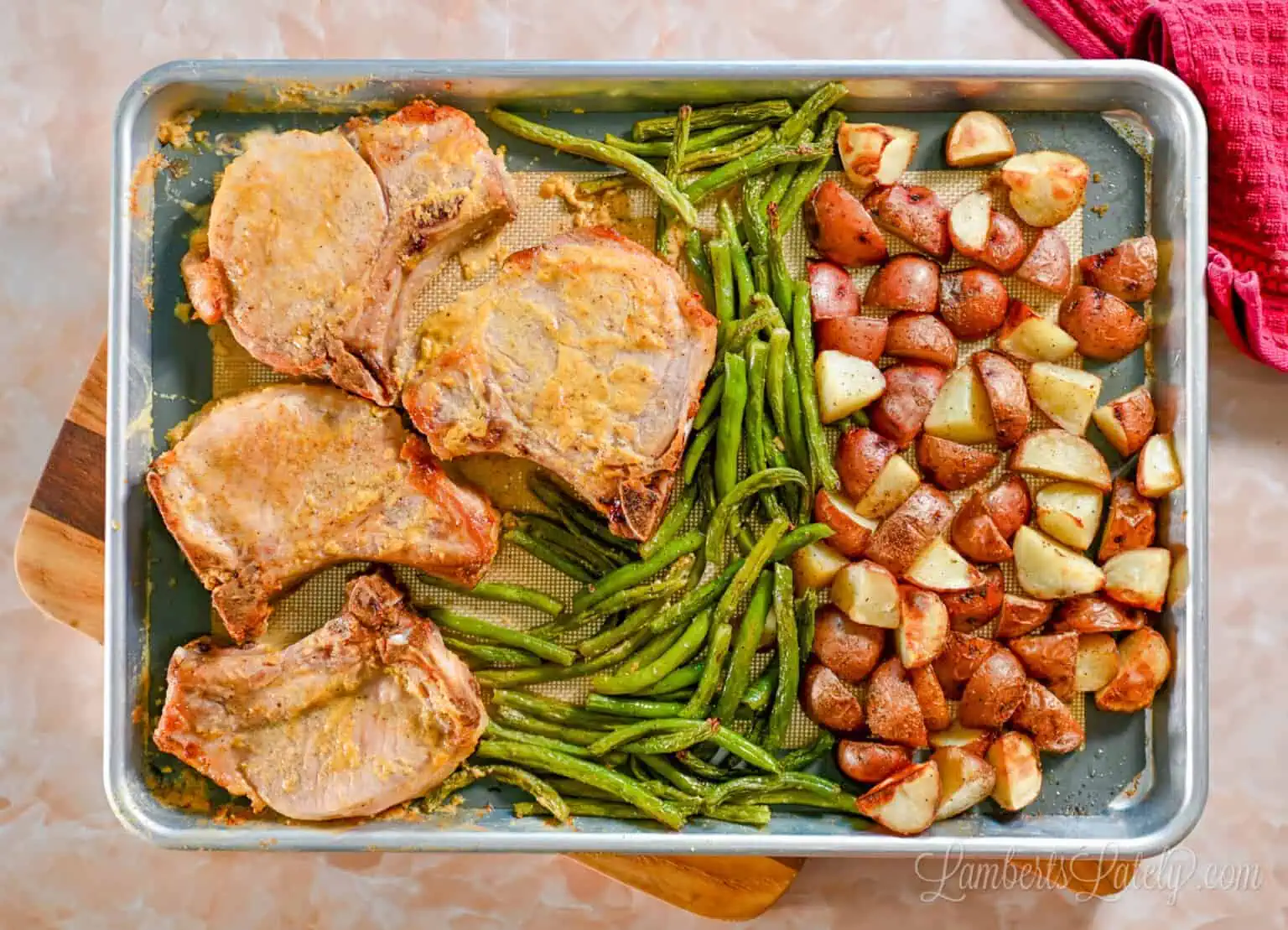 a sheet pan with baked pork chops, crispy baked potato pieces, and whole green beans after cooking.