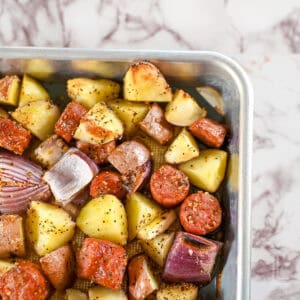 sheet pan sausage and potatoes with red onions on a baking sheet.