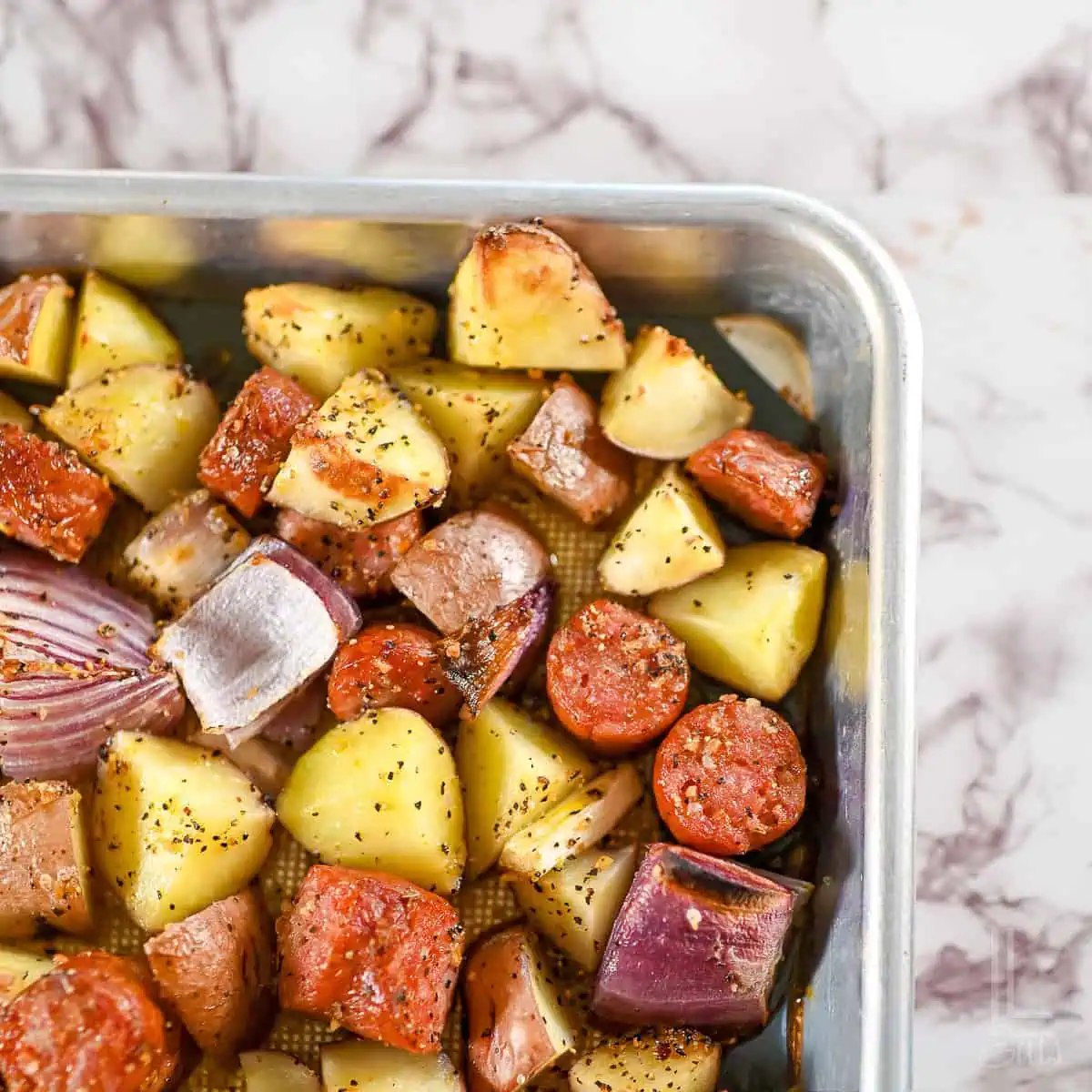 sheet pan sausage and potatoes with red onions on a baking sheet.