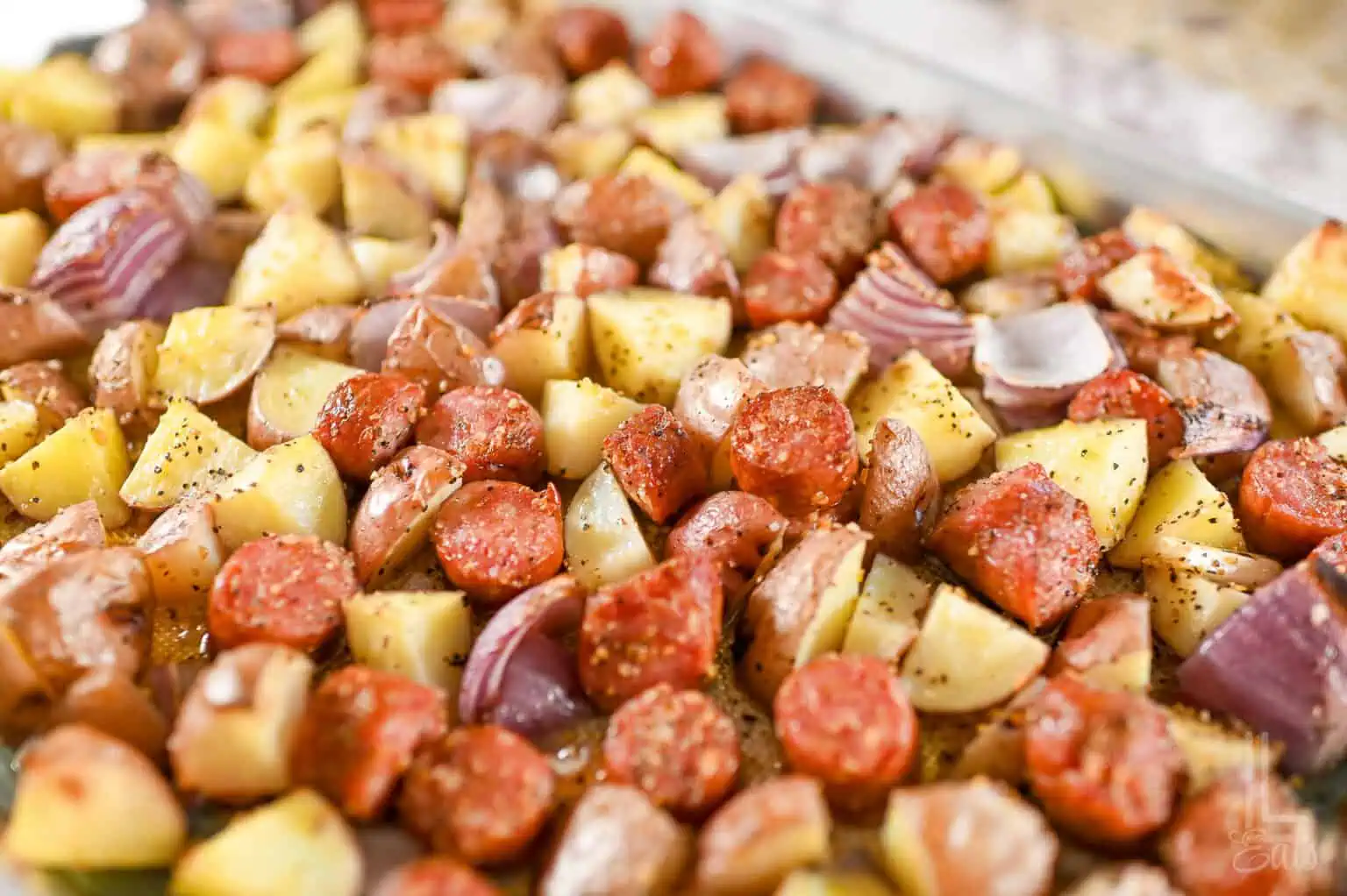 roasted sausage, potatoes, and red onions on a sheet pan.