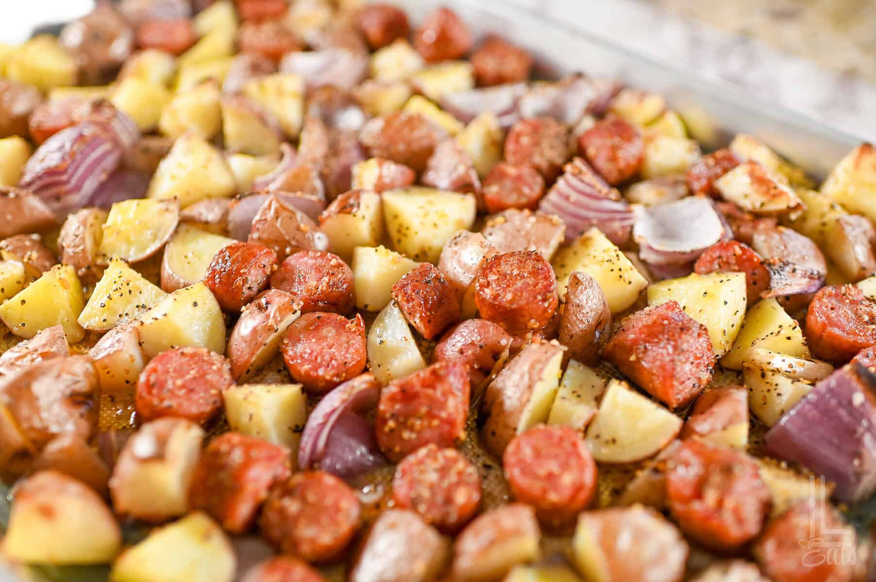 roasted sausage, potatoes, and red onions on a sheet pan.