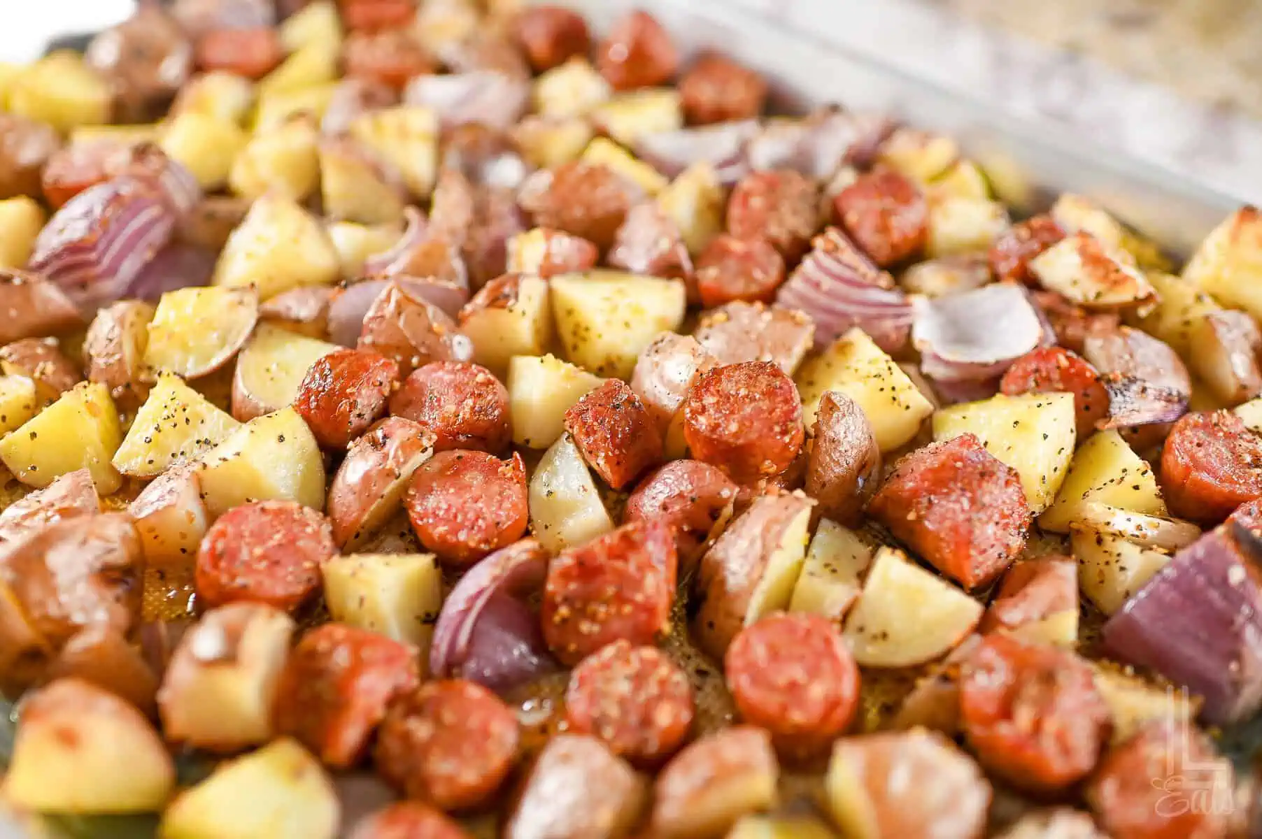 roasted sausage, potatoes, and red onions on a sheet pan.
