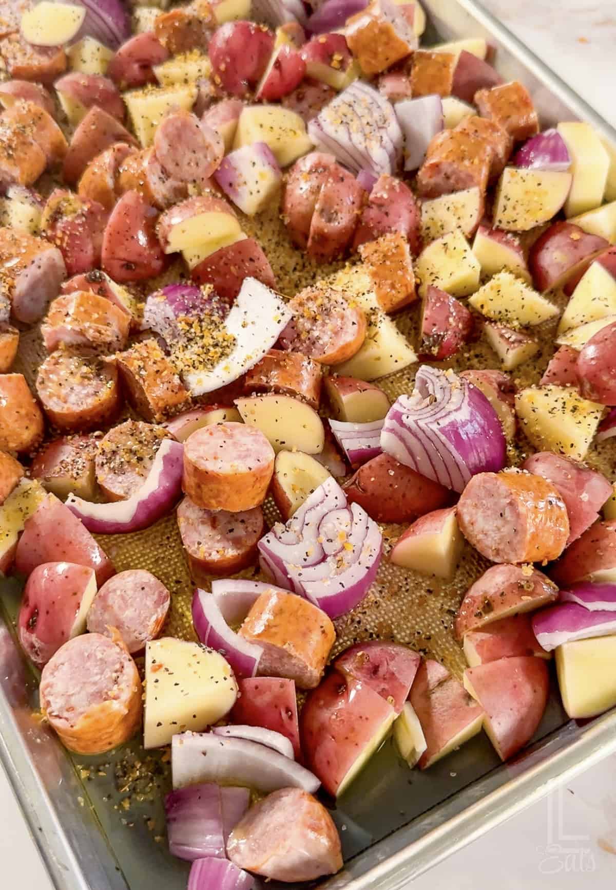 Sheet pan with sausage, potatoes, and onions ready for roasting.