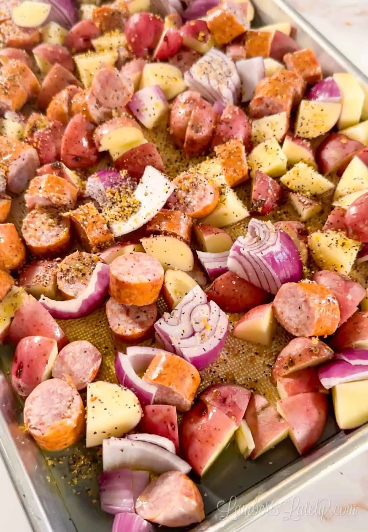 sausage, potatoes, and onion tossed with olive oil and seasoning on a sheet pan.