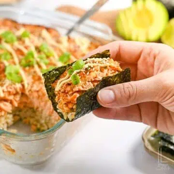 holding a bite of spicy salmon sushi bake in a piece of nori seaweed paper.