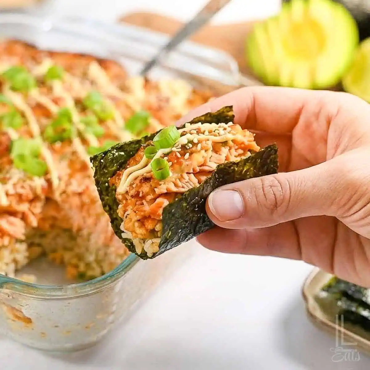 holding a bite of spicy salmon sushi bake in a piece of nori seaweed paper.