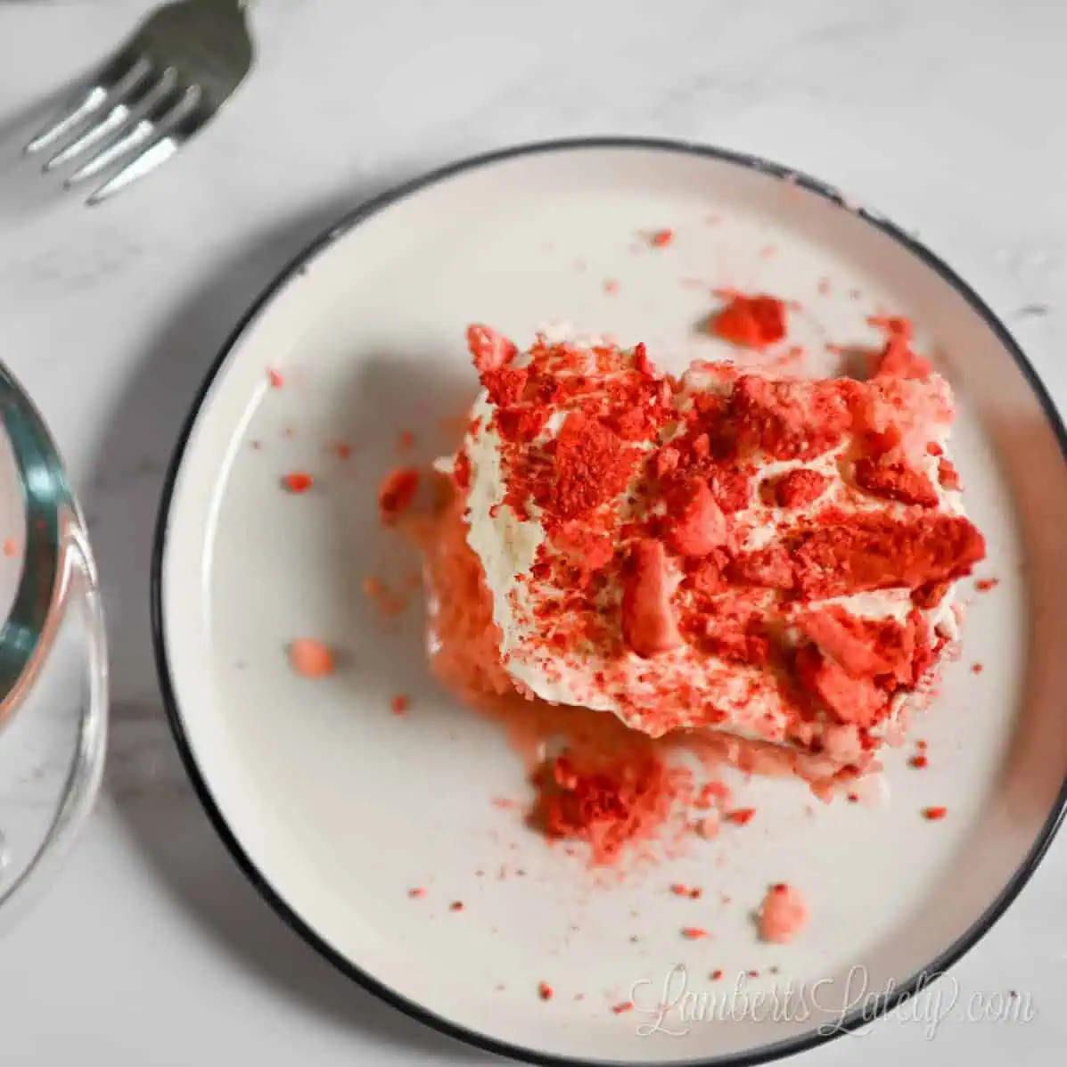 a piece of strawberry tres leches cake on a plate next to the baking dish of cake.