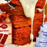 Stacked red velvet waffles with cream cheese icing and cake mix label in background.