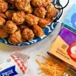 Cream cheese sausage balls on a blue plate with shredded cheese and ingredients nearby.