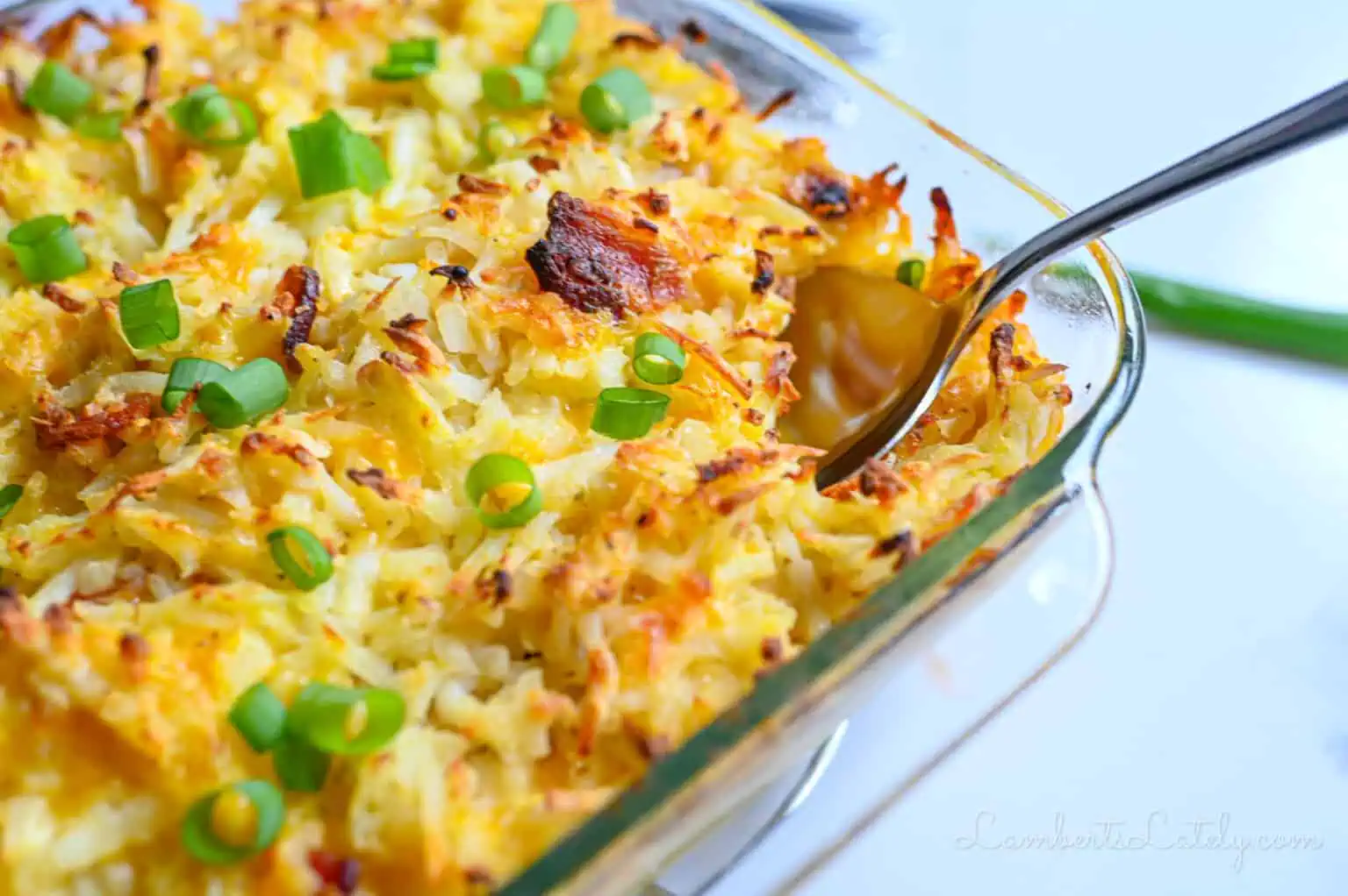 Cheesy baked potato casserole with green onions in a glass dish.