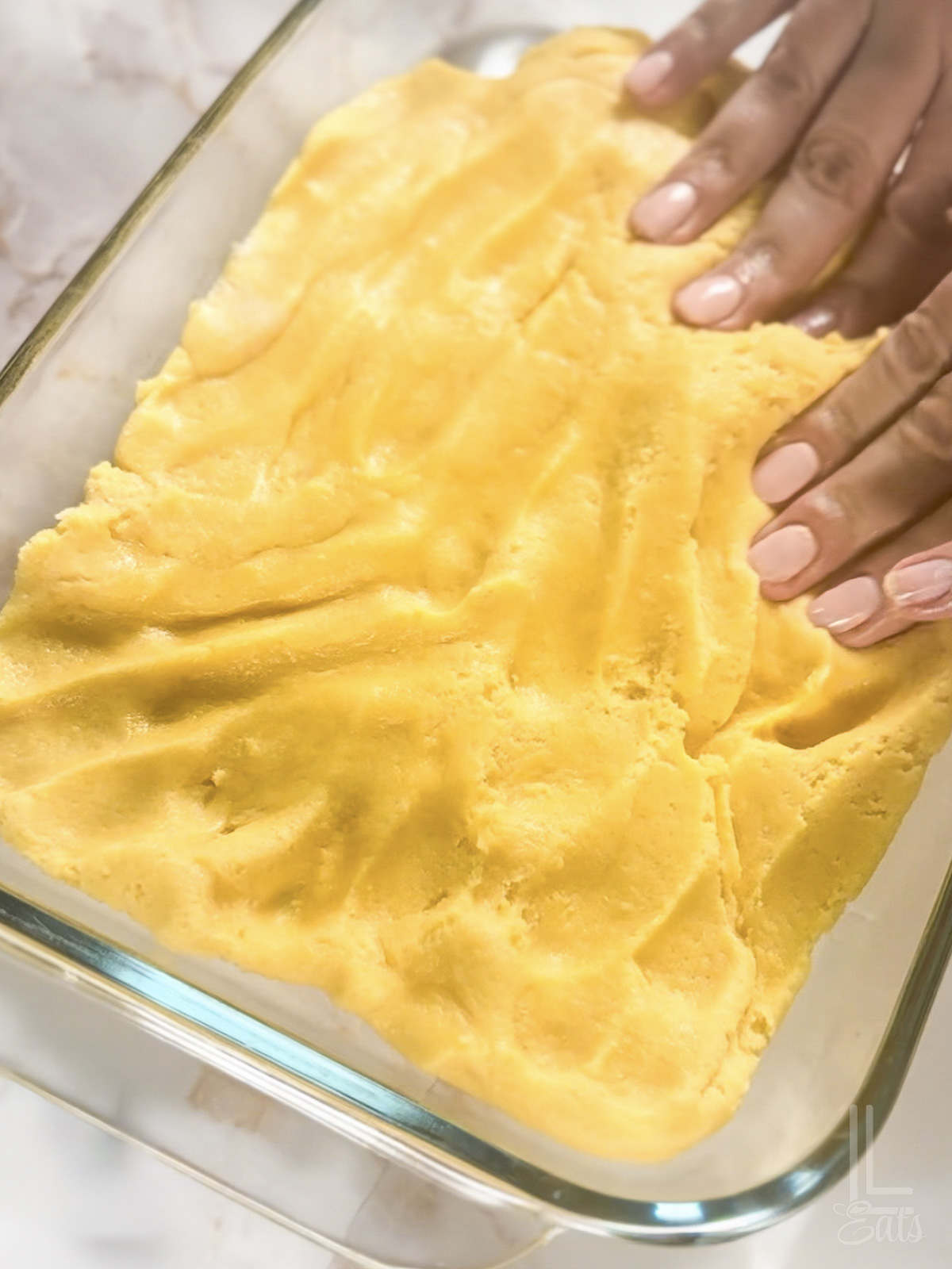 pressing a yellow blondie mixture into a glass baking dish with hands.