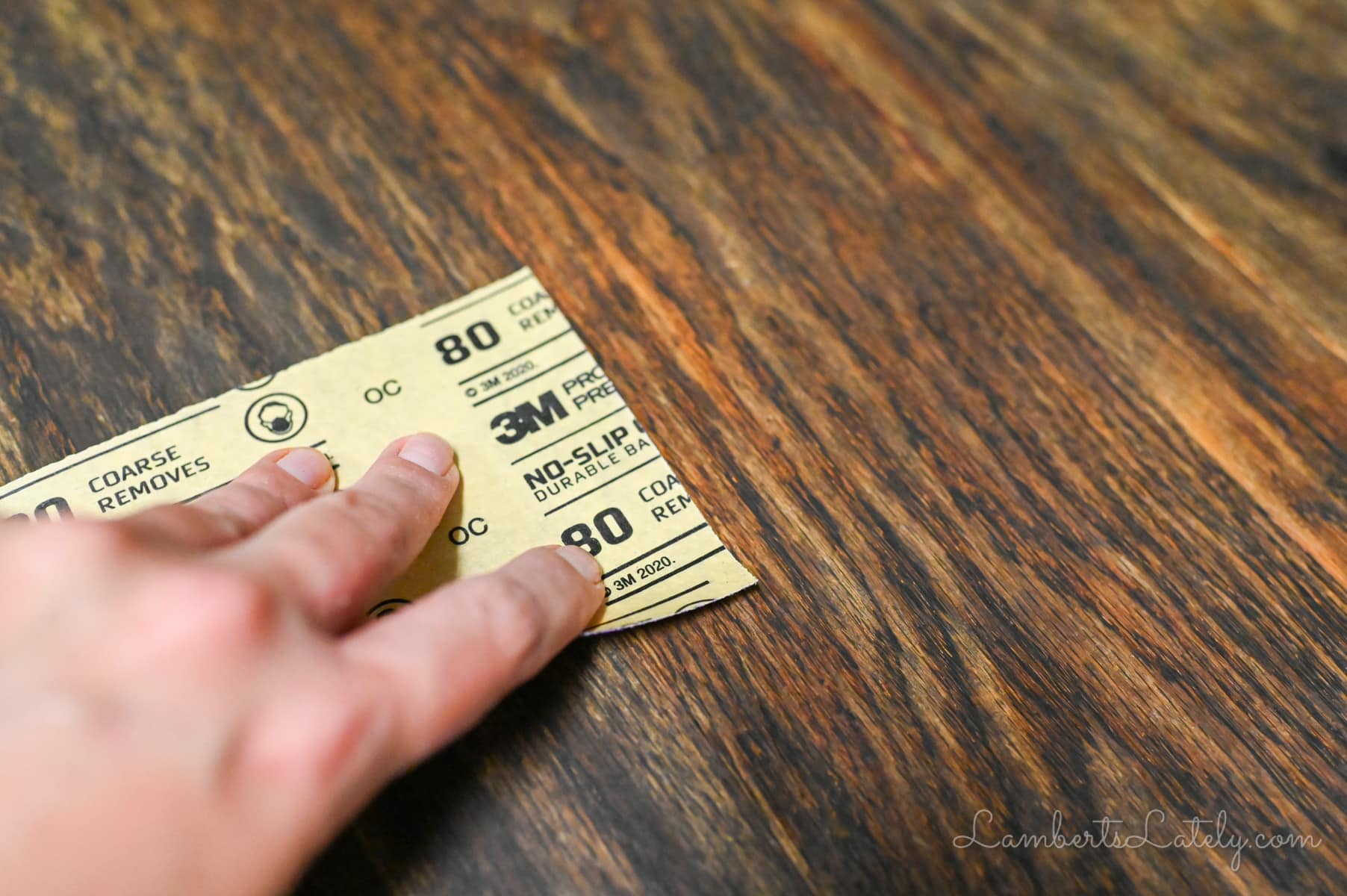 sanding a wood table with a piece of sandpaper.
