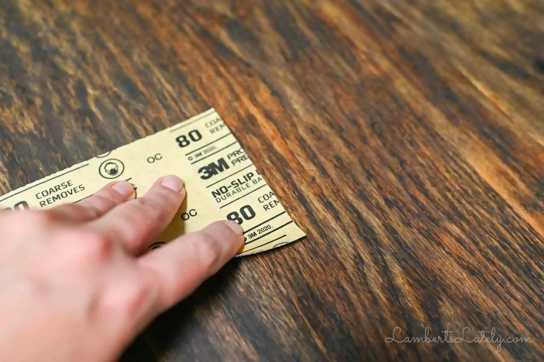 sanding a wood table with a piece of sandpaper.