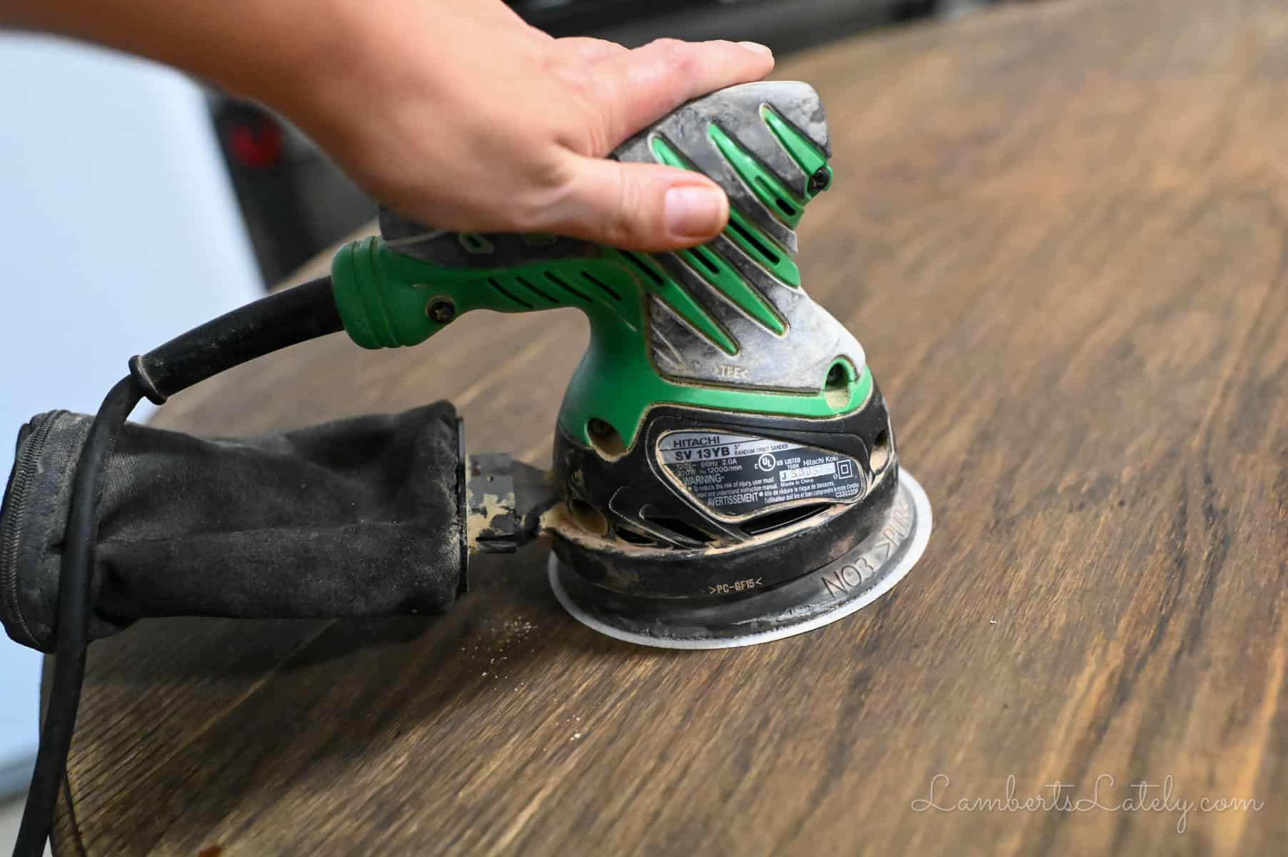 using an orbital sander on a wood table.