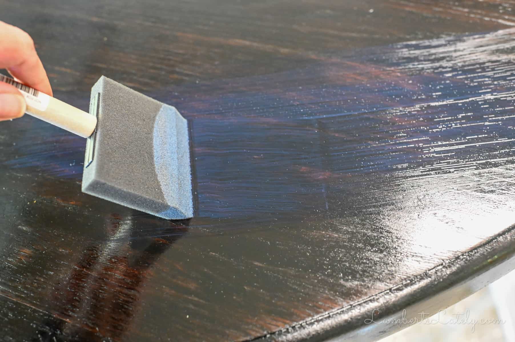 brushing polyurethane onto a stained table with a sponge brush.