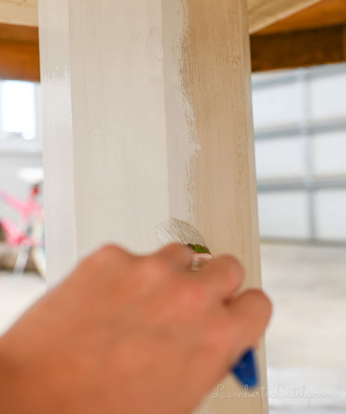 painting a light paint on the base of a wood table.