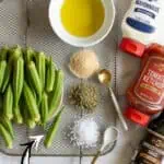 Crispy air fryer okra pods with seasonings and condiments on a wire rack.