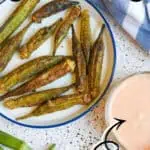 Crispy air fryer okra pods served with dipping sauce on a white plate.