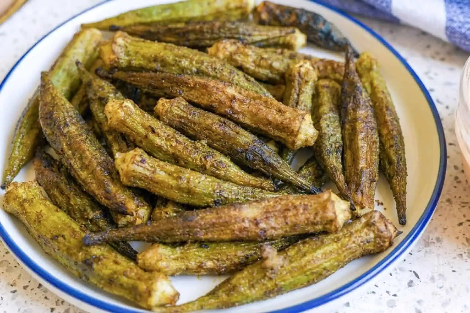 crispy, seasoned air fryer okra stacked on a plate.