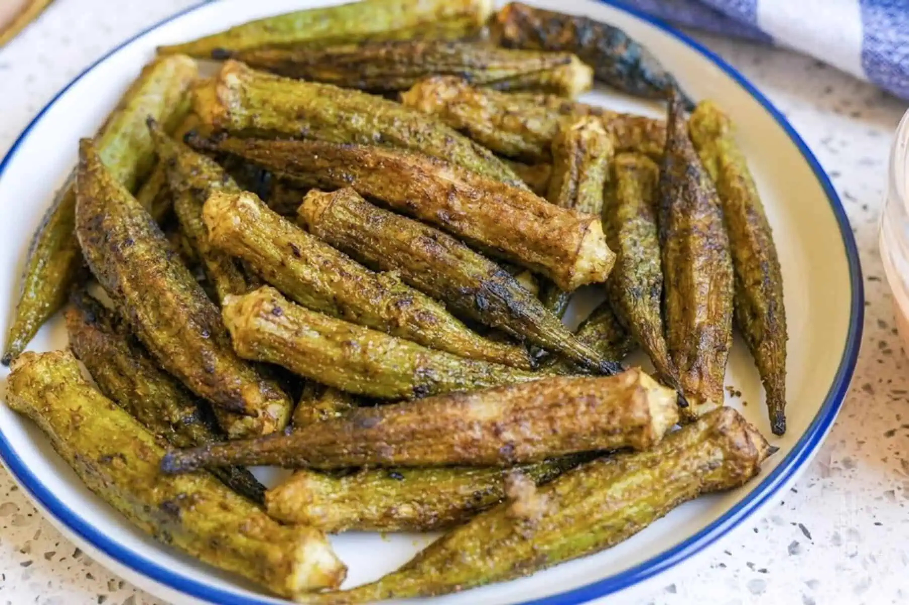 crispy, seasoned air fryer okra stacked on a plate.