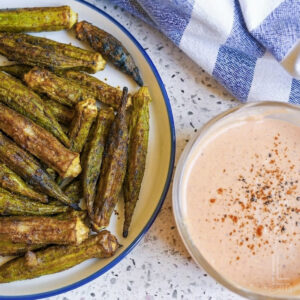 whole okra pods after removing from the air fryer, with a crispy browned exterior, next to a bowl of pink dipping sauce.