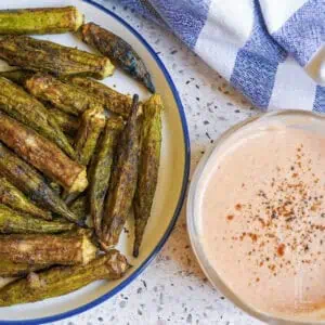 whole okra pods after removing from the air fryer, with a crispy browned exterior, next to a bowl of pink dipping sauce.