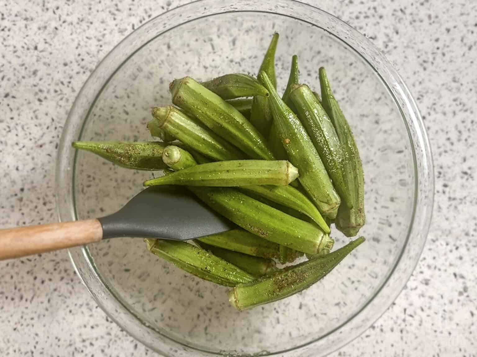 tossing the whole okra pods with oil and seasonings in a glass bowl.