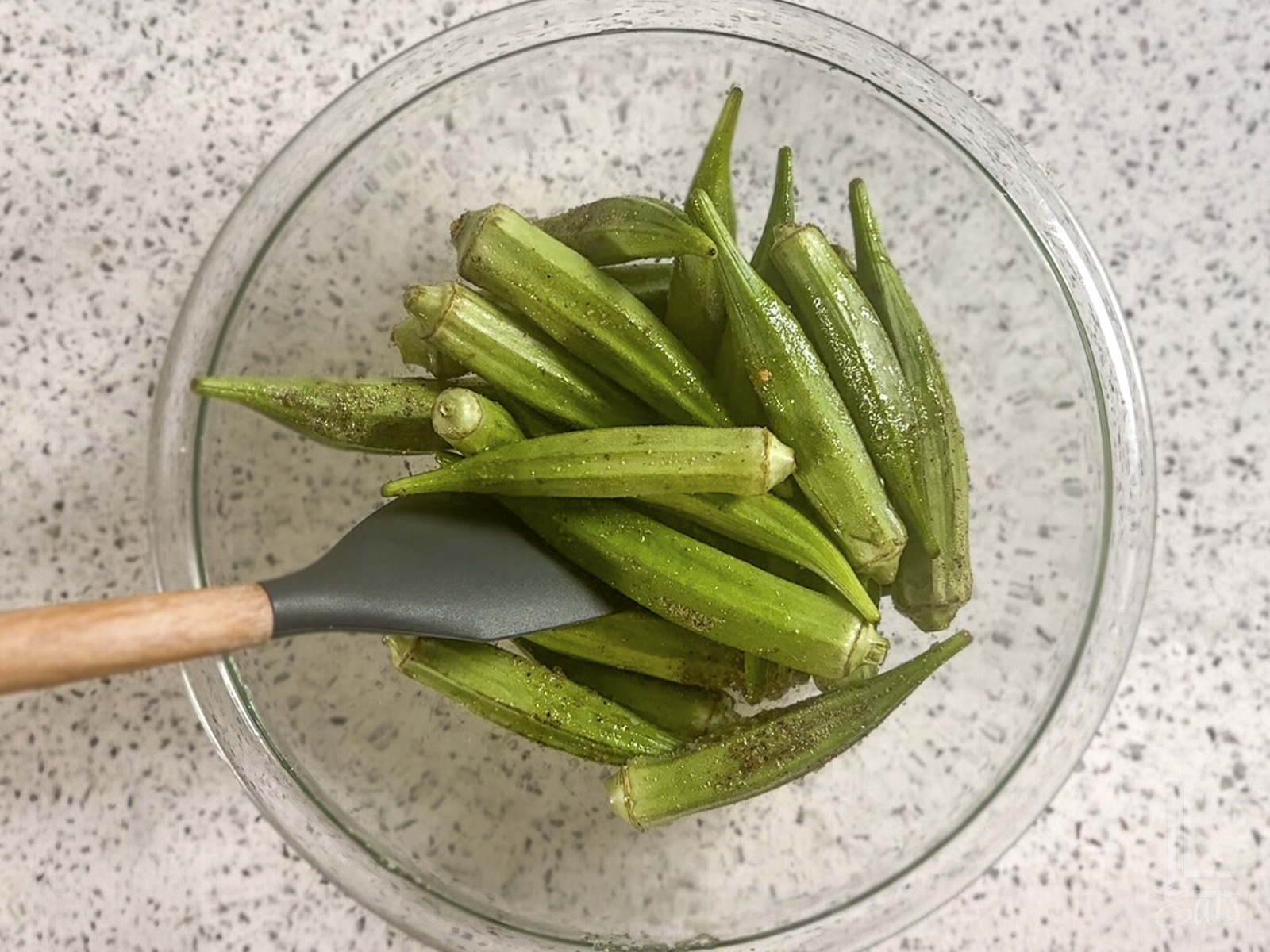 tossing the whole okra pods with oil and seasonings in a glass bowl.