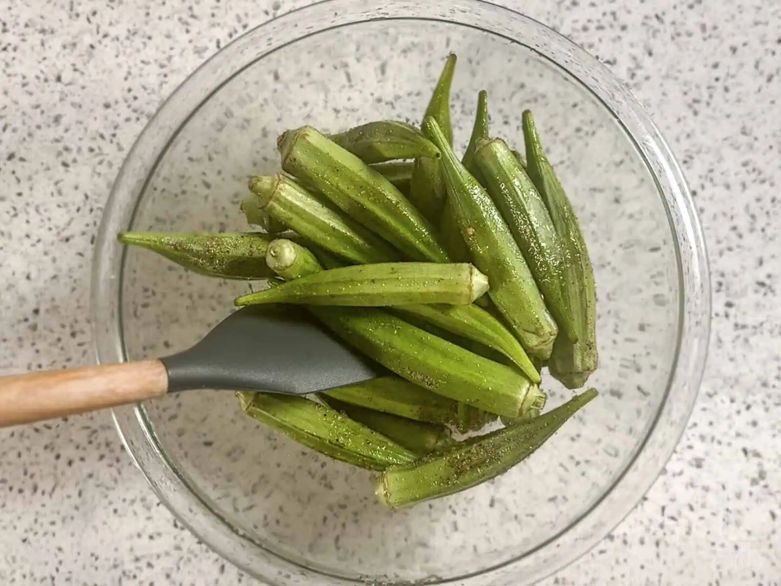 tossing the whole okra pods with oil and seasonings in a glass bowl.