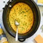 Delicious crock pot corn casserole garnished with herbs in a black slow cooker.