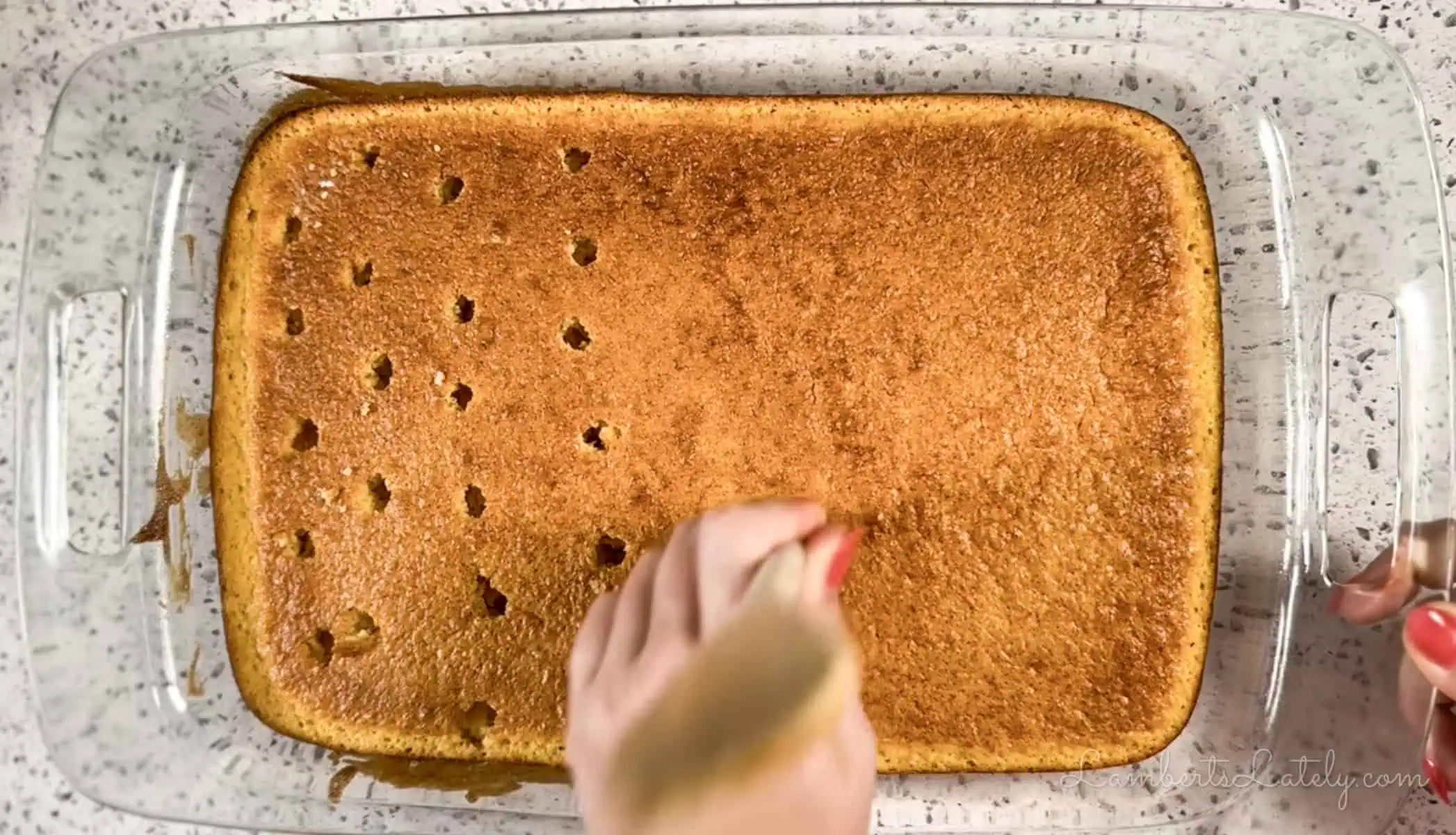 poking holes in a sheet cake with the back of a wooden spoon.