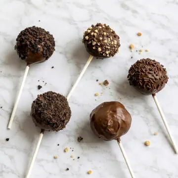 Chocolate cake pops with various toppings and chocolate coating on a marble surface.