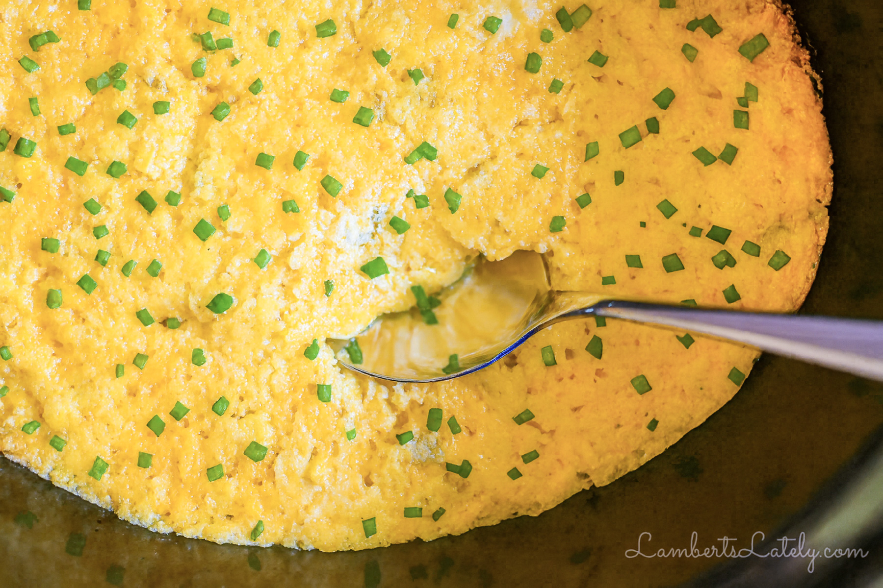 crock pot corn casserole in a slow cooker, with a spoon.