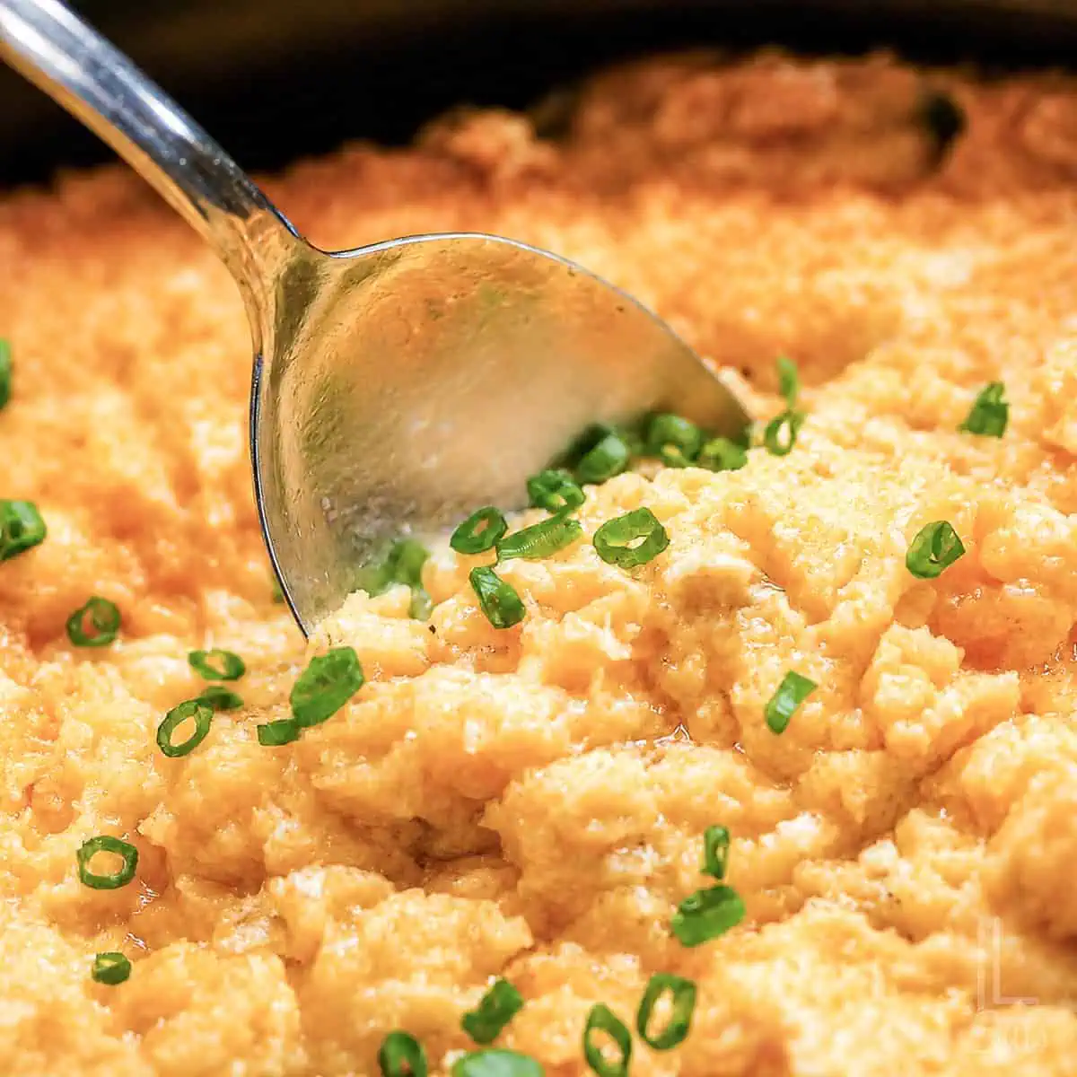 spoon in corn casserole in a crock pot, garnished with green onions.