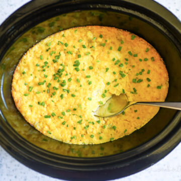 crock pot corn casserole in a slow cooker, with a spoon.