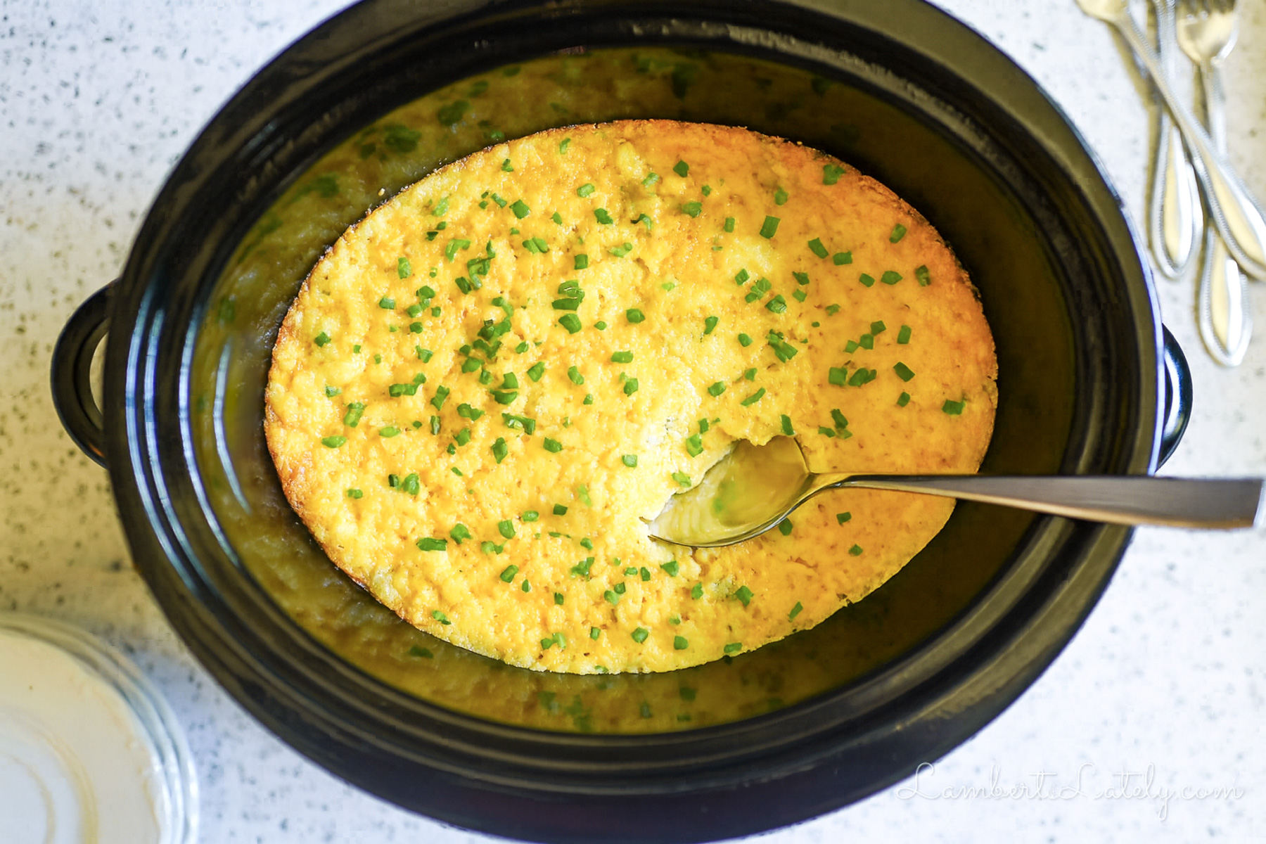 crock pot corn casserole in a slow cooker, with a spoon.