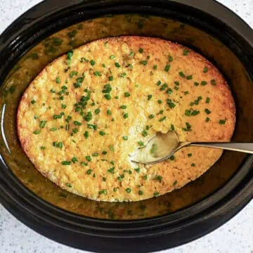 crock pot corn casserole in a slow cooker, with a spoon.