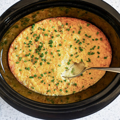 crock pot corn casserole in a slow cooker, with a spoon.