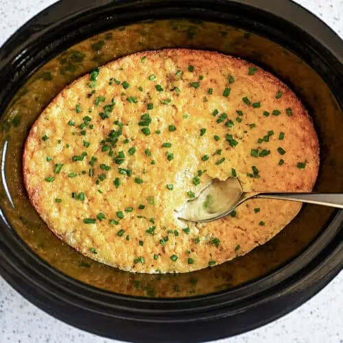 crock pot corn casserole in a slow cooker, with a spoon.