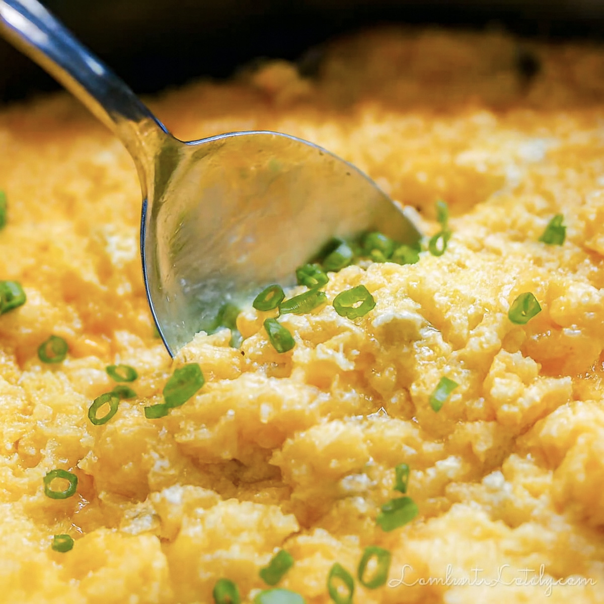 spoon in corn pudding, garnished with green onions.