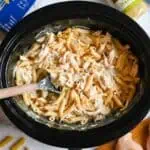 Creamy Italian chicken pasta in a black slow cooker with ingredients around.