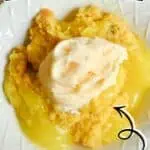 Lemon dump cake with a dollop of whipped cream on top, featuring fresh lemons in background.