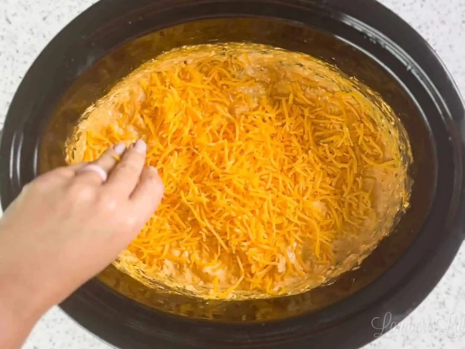 Shredded cheddar added over buffalo chicken dip in a slow cooker