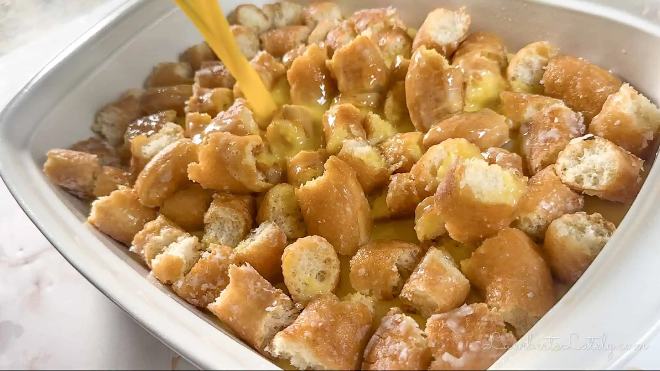 pouring custard over donut pieces in a casserole dish.