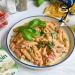 Baked Boursin cheese penne pasta with basil and cherry tomatoes on a white plate.
