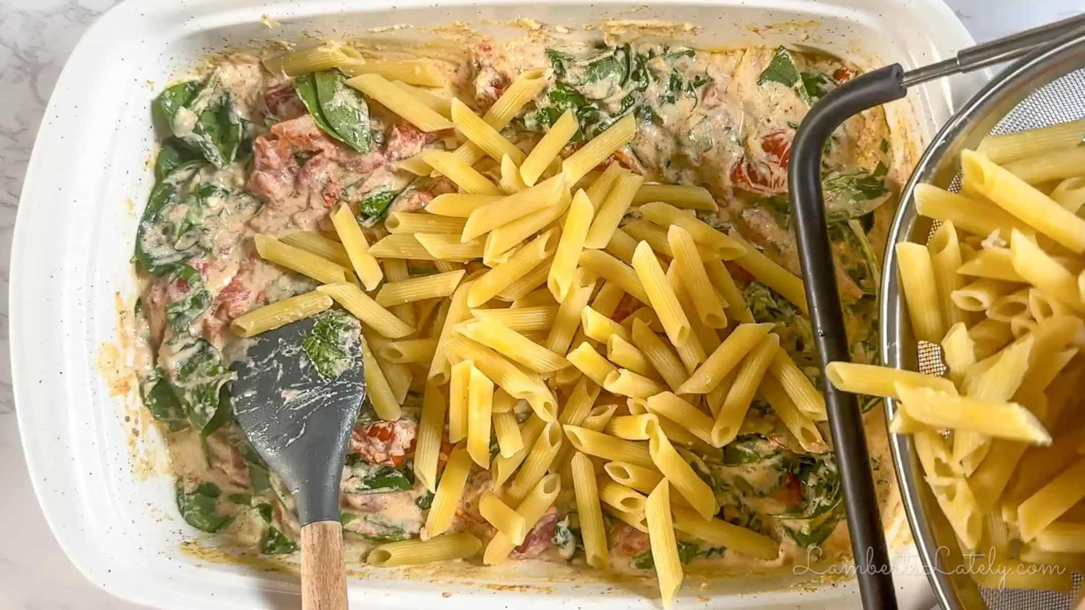 adding pasta to the boursin tomato cheese sauce in a baking dish.