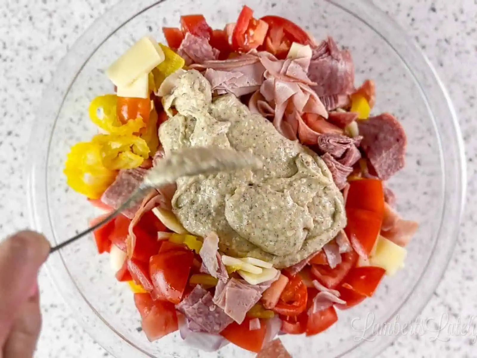 spooning dressing over meat, cheese, and veggies in a bowl.