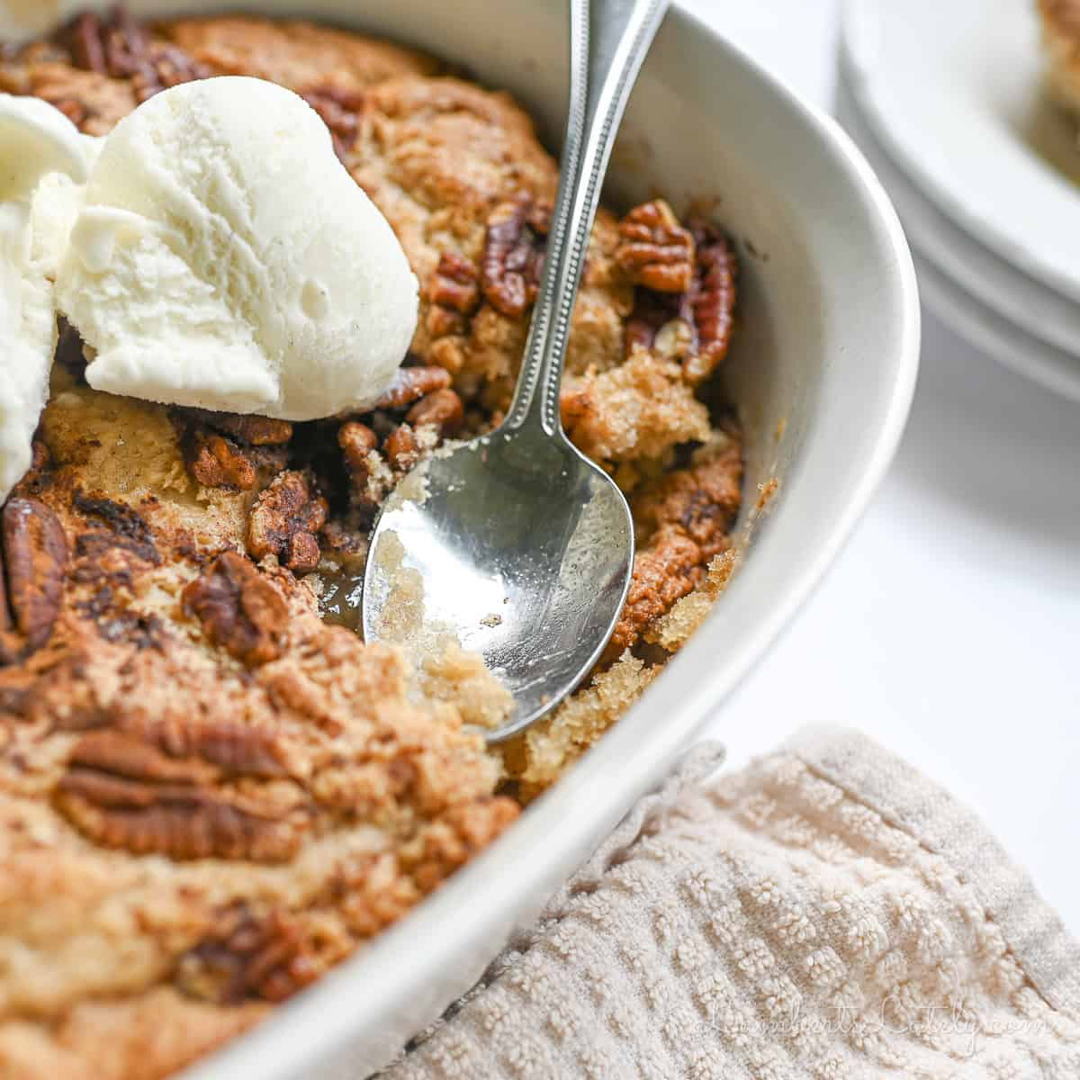 spoon in a pecan pie cobbler dish, topped with ice cream.