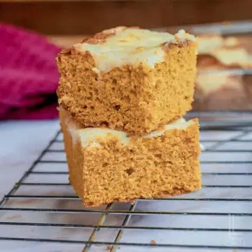 two pumpkin cake mix bars stacked on a baking rack, topped with a cream cheese swirl.